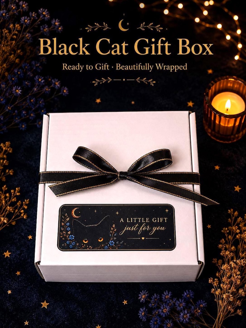 K&ouml;nnte beinhalten: Eine wei&szlig;e, rechteckige Geschenkbox, die mit einem schwarzen Band mit goldenem Rand verschlossen ist. Ein rechteckiges Etikett auf der Vorderseite zeigt die Silhouette einer schwarzen Katze mit leuchtend orangen Augen, blauen Blumen, einem Halbmond und dem Text A LITTLE GIFT just for you.