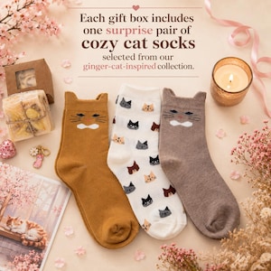 K&ouml;nnte beinhalten: Drei Paar Socken mit Katzenmotiven. Ein Paar ist senfgelb mit Katzenohren und Schnurrhaaren, eines ist wei&szlig; mit kleinen Katzengesichtern und eines ist taupefarben mit Katzenohren und Schnurrhaaren. Der Text lautet: Each gift box includes one surprise pair of cozy cat socks selected from our ginger-cat-inspired collection.