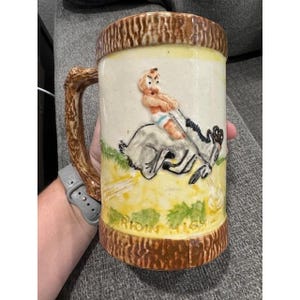 May include: A white ceramic mug with a black handle and the text "But First, Coffee" in a black, handwritten-style font. The mug is on a white surface.