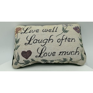 Könnte beinhalten: Rechteckiges Zierkissen mit dem gestickten Text "Live well, Laugh often, Love much". Das Kissen hat einen beigen Hintergrund mit floralen und herzförmigen Akzenten. Die Kanten sind mit dunkelgrünem Stoff eingefasst.