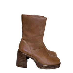 May include: A pair of brown leather boots with a block heel and platform sole. The boots have a rounded toe and a mid-calf shaft. The heel is approximately 3 inches high.