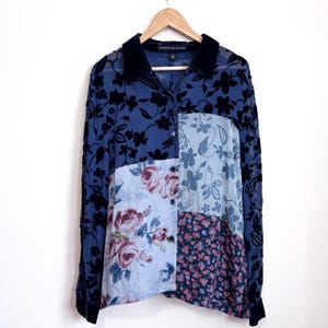May include: A long-sleeve button-down shirt featuring a patchwork design with sheer navy blue fabric adorned with black floral velvet flocking, light blue panels with rose prints, and a smaller floral pattern, finished with a solid navy collar.