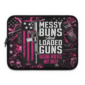 Puede incluir: Funda negra para portátil con un diseño que presenta armas, calaveras y el texto "Messy Buns and Loaded Guns, Raising Wolves Not Sheep". El diseño incluye una bandera americana rosa y negra.