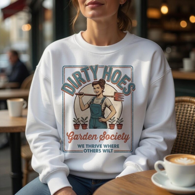 May include: White sweatshirt featuring the text "DIRTY HOES" above an illustration of a woman with a gardening tool. The graphic also includes "Garden Society" and "WE THRIVE WHERE OTHERS WILT".