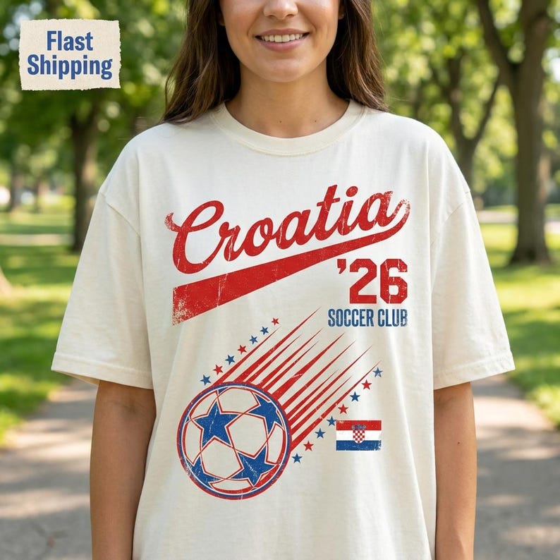 May include: An off-white short-sleeve t-shirt featuring the red text Croatia, the number 26, and the words SOCCER CLUB. Below, a graphic shows a soccer ball with blue star patterns and red motion lines, accompanied by a small Croatian flag icon.