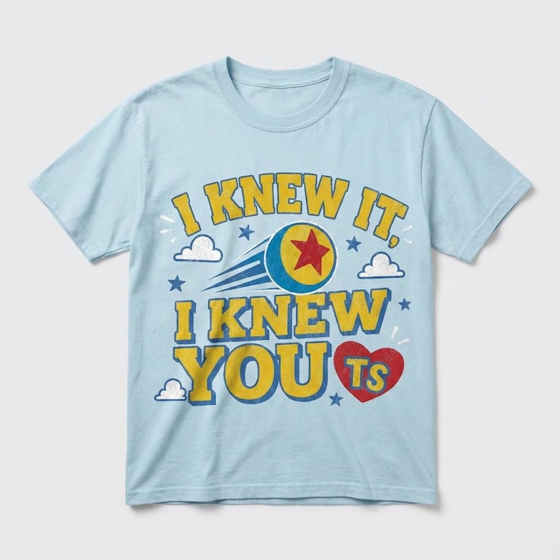 K&ouml;nnte beinhalten: Ein hellblaues Kurzarm-T-Shirt mit dem gelben Schriftzug I KNEW IT, I KNEW YOU und einem roten Herz, das die Buchstaben TS enth&auml;lt. Das Design zeigt einen blauen Ball mit einem roten Stern, kleine wei&szlig;e Wolken und blaue Sterne als Grafikdruck.