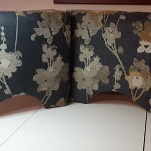May include: A decorative valance with a floral pattern. The fabric features a dark blue background with a repeating design of beige, white, and light brown flowers and branches. The valance has a curved bottom edge.