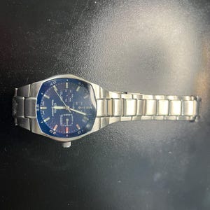 May include: A silver-tone stainless steel wristwatch with a dark blue dial, featuring a metal link bracelet, a rotating bezel with numerical markers, and the text "SIERA Water Resistant" printed on the face with multiple sub-dials and hands.