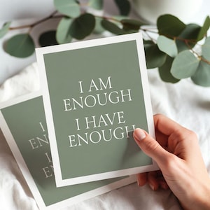 Peut inclure: Deux cartes avec un fond vert sauge et des bordures blanches. Les cartes portent le texte "I AM ENOUGH I HAVE ENOUGH" dans une police sans-serif épurée. Les cartes sont sur une surface blanche, avec des feuilles vertes en arrière-plan.