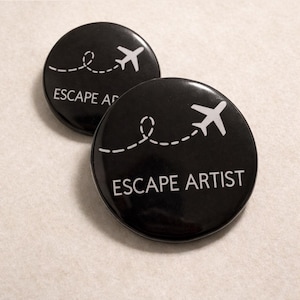 May include: Two black round buttons with white text and graphics. Each button features a white airplane icon and the words "ESCAPE ARTIST". A dotted line traces a path from the airplane.