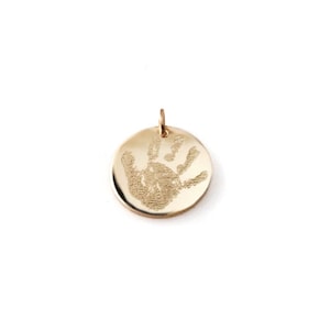 May include: Gold-toned pendant featuring a handprint design. The pendant is round and has a smooth, polished finish.