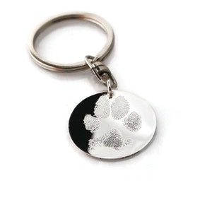 May include: Silver keychain with a round charm featuring a paw print. The paw print is made from a pet's actual paw.