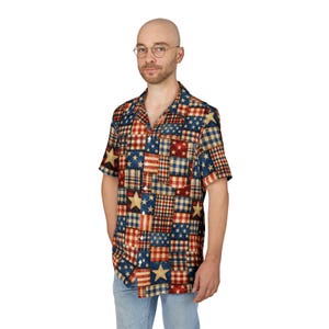 May include: Short-sleeved shirt with a patchwork design featuring stars, stripes, and plaid patterns in red, blue, and beige. The shirt has a classic collar and a chest pocket. The shirt is made of a lightweight fabric.