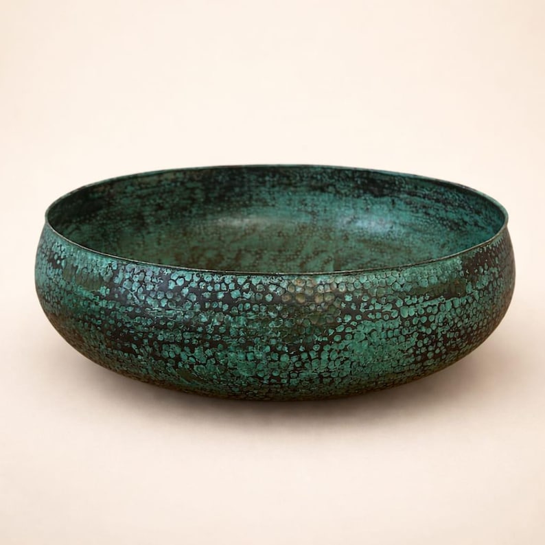 May include: A handcrafted, round bowl with a textured surface and a distressed, verdigris finish. The bowl's exterior features a mottled pattern of dark and light green hues, creating a unique, aged appearance. The bowl is ideal for decorative purposes.