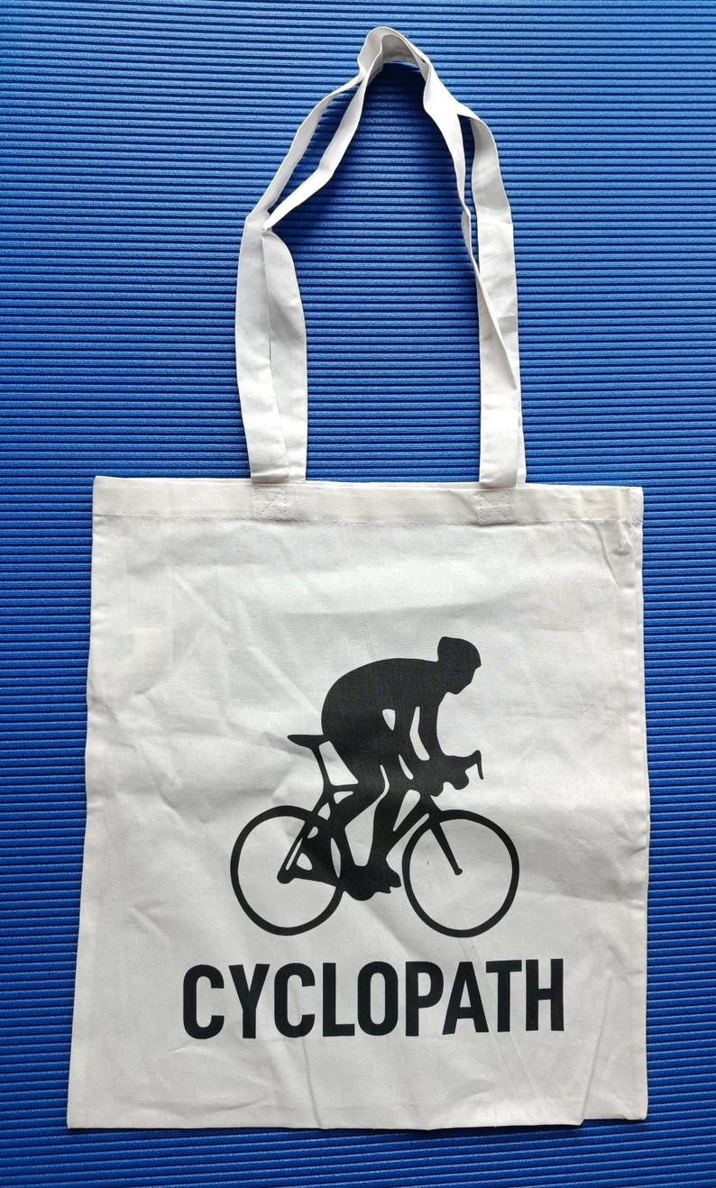 Puede incluir: Bolso tote blanco con una silueta negra de un ciclista en bicicleta. La palabra "CYCLOPATH" est&aacute; impresa en negro debajo. El bolso tiene dos asas blancas y est&aacute; sobre un fondo azul.