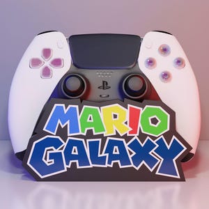 Op de afbeelding: Een wit en zwarte gamecontroller met de tekst "MARIO GALAXY". De controller heeft een PlayStation-logo en een symmetrisch ontwerp met knoppen aan elke kant. De achtergrond is een verloop van paars en rood.