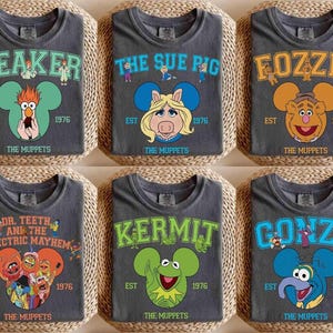 May include: Six charcoal gray t-shirts featuring Muppets characters: Beaker, Miss Piggy, Fozzie Bear, Dr. Teeth and the Electric Mayhem, Kermit, and Gonzo. Each shirt has the character's name, the year 1976, and "The Muppets" printed on it.