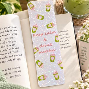 May include: A rectangular bookmark with a holographic finish featuring a repeating pattern of green matcha drinks with pink heart accents and the text Keep calm & drink matcha in pink script lettering centered on the surface.