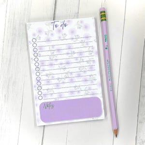 May include: A floral-patterned To-Do list notepad with a purple Notes section and a matching purple pencil. The notepad has a floral design in shades of purple and gray. The pencil is light purple with green and yellow accents.