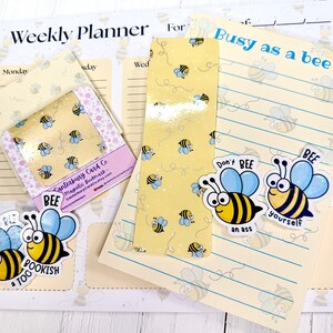 May include: A stationery set featuring a weekly planner, a lined notepad with the text Busy as a bee, and a magnetic bookmark. The items are decorated with yellow and black bee patterns and include die-cut stickers with the text Don't BEE an ass, BEE yourself, and Don't BEE too BOOKISH.