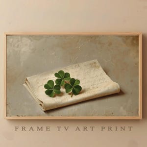 May include: A framed art print showing three green shamrocks on a folded, vintage letter with handwritten text. The frame is light-coloured wood. The words "FRAME TV ART PRINT" are at the bottom of the print.