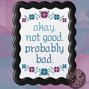 Può includere: Ricamo a punto croce in una cornice nera ondulata. Il testo recita "okay. not good. probably bad." in blu-azzurro. Accenti floreali in blu-azzurro, viola e rosa in alto e in basso. Lo sfondo è un acquerello rosa e blu.