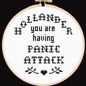Może przedstawiać: Obręcz do haftu krzyżykowego z napisem "HOLLANDER you are having PANIC ATTACK" czarną nicią na białym materiale. Projekt zawiera serce i kwiatowe akcenty. Widoczna jest drewniana obręcz.