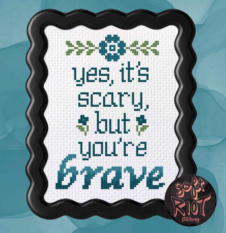 Pu&ograve; includere: Ricamo a punto croce in una cornice nera ondulata. Il testo recita "yes, it's scary, but you're brave" in verde acqua e verde. Una spilla rotonda con la scritta "soft riot stitchery" si trova nell'angolo in basso a destra.