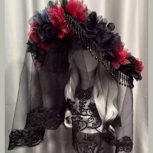 Könnte beinhalten: Ein schwarzer Schleier mit einem floralen Kopfschmuck. Der Kopfschmuck hat rote, schwarze und blaue Stoffblumen mit Perlenakzenten. Der Schleier hat eine Spitzenborte.