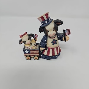 Puede incluir: Una taza de cerámica blanca con un asa negra y el texto "But First, Coffee" en negrita negra. La taza está sobre una superficie de madera. La taza mide aproximadamente 10 cm de alto.