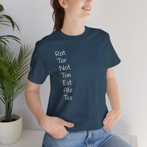 May include: Navy blue t-shirt with white text that reads "Rat Tar Not Ton Eat Ate Tea". The shirt is a crew neck and is being worn by a person.