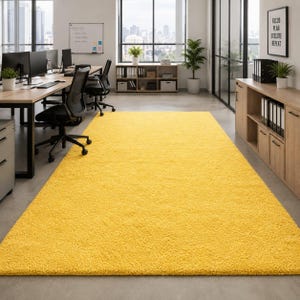 May include: A large, rectangular, solid yellow area rug with a thick, plush, shaggy texture covering the floor of an office space. The rug features a uniform, vibrant yellow color throughout its entire surface, providing a soft contrast to the room.