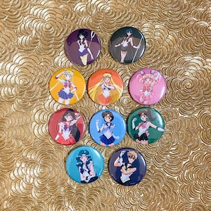 May include: Nine round pinback buttons featuring characters from the anime Sailor Moon. The buttons are colourful and feature different characters in various poses.