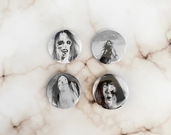 May include: Four black and white horror-themed button pins. Each pin features a different image of a scary face or figure. One pin has the text "Scary Spells". The pins are round and have a glossy finish.