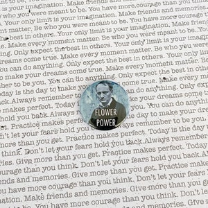 May include: A blue and white button with the words "Flower Power" in white text. The button features a black and white image of a man with a mustache and a flower behind him.