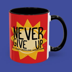 May include: A ceramic coffee mug with a red exterior, black interior, and a black handle. The mug features the text "NEVER GIVE UP" in black letters, set against a yellow burst design. The phrase "ON YOUR CRIPPLING ADDICTIONS" is below the main text.