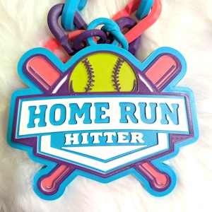 May include: A colorful softball-themed pendant with the words "HOME RUN HITTER" in white and blue. The pendant features a yellow softball and crossed bats, with a chain of pink, blue, and purple links.