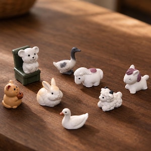 May include: A collection of miniature animal figurines including a white bear sitting on a green chair, a brown cat, a white rabbit, a grey and white goose, a white pony, a white sheep, a white duck, and a small white unicorn with a purple mane.