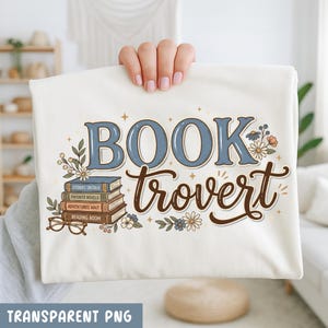 Op de afbeelding: Crèmekleurig T-shirt met de woorden "BOOKtrovert" in blauwe en bruine letters. Het ontwerp bevat een stapel boeken, bloemen en een bril. De tekst "TRANSPARENT PNG" staat onderaan.