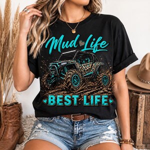 May include: Black t-shirt with the words "Mud Life" and "Best Life" in turquoise. The graphic features a turquoise and leopard print off-road vehicle splashing through mud. The shirt has short sleeves and a crew neck.
