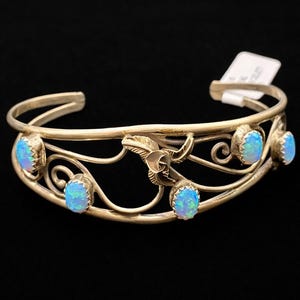 May include: Silver-toned cuff bracelet with an open design. The bracelet features five oval, light blue opal stones and decorative floral and swirl accents. The bracelet is set against a black background.