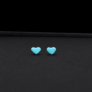 May include: A pair of small, smooth, bright turquoise blue heart-shaped stud earrings. Each earring features a simple, solid-colored heart design with a rounded surface, presented as a matching set of two individual pieces for earlobe wear.
