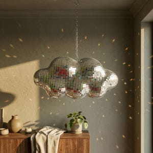 May include: A cloud-shaped hanging pendant light covered in small, reflective silver mirror tiles. The fixture is suspended by a thin metal chain and casts scattered, multi-colored light reflections onto the surrounding walls and surfaces.