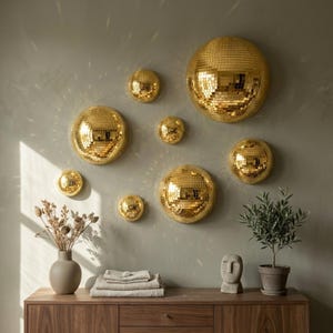 May include: A collection of gold disco balls of varying sizes mounted on a light green wall. The mirrored surfaces reflect light, creating a sparkling effect. The balls are arranged in a visually appealing pattern, adding a touch of glamour to the space.