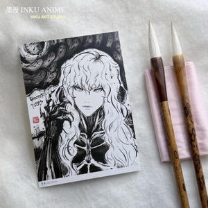 Puede incluir: Una impresión artística de anime en blanco y negro, que representa a un personaje con cabello largo y ondulado y una expresión seria. Dos pinceles de caligrafía con mangos de madera y puntas blancas descansan sobre una tela rosa. Incluye texto japonés y "INKU ANIME".