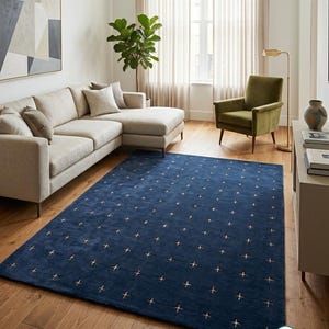 Könnte beinhalten: Ein rechteckiger Teppich in tiefem Marineblau mit einem sich wiederholenden Gittermuster aus kleinen, hellen Kreuzsymbolen. Der Teppich hat eine weiche, strukturierte Oberfläche und liegt auf einem hellen Holzboden in einem Wohnzimmer.