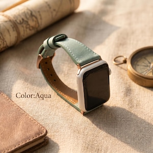 May include: A smartwatch with a white casing and an aqua leather strap featuring rose gold hardware. The strap has visible stitching along the edges and a buckle closure. The text Color:Aqua is printed on the surface near the watch.