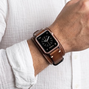 Könnte beinhalten: Eine Smartwatch mit roségoldenem Metallgehäuse und schwarzem Digitaldisplay, das eine Kompassanzeige, die Uhrzeit 10:09 Uhr und eine Temperatur von 9 Grad zeigt. Sie hat ein breites, braunes Leder-Manschettenarmband mit sichtbaren cremefarbenen Nähten.