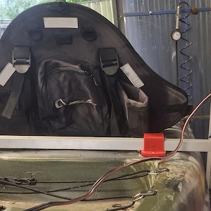 Könnte beinhalten: Ein schwarzer Kajaksitz mit mehreren Taschen und Gurten ist auf einem Kajak montiert. Ein weißes Gerät mit dem Wilson-Logo ist am Kajak befestigt. Das Gerät ist mit Drähten und einer Metallstange mit dem Kajak verbunden.