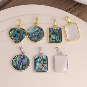 May include: A collection of seven pendants featuring iridescent abalone shell and smooth white mother-of-pearl inlays. The set includes heart, circular, and rectangular shapes set in gold-toned and silver-toned metal frames with attached bails.